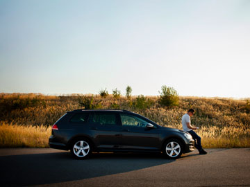 Mann setzt sich auf die Motorhaube ab, um zu telefonieren